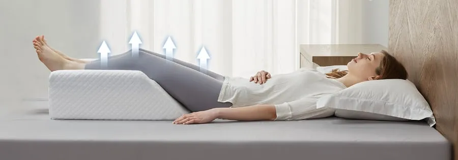 A woman lying on her back with her legs raised on a wedge-shaped leg elevation pillow